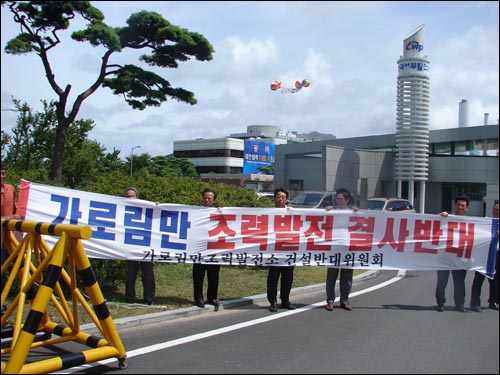 태안화력 정문에서 반대위원회가 시위를 벌이고 있는 가운데 시위대 뒤로 태안화력 7.8호기 축하 애드벌룬이 날고 있다. 